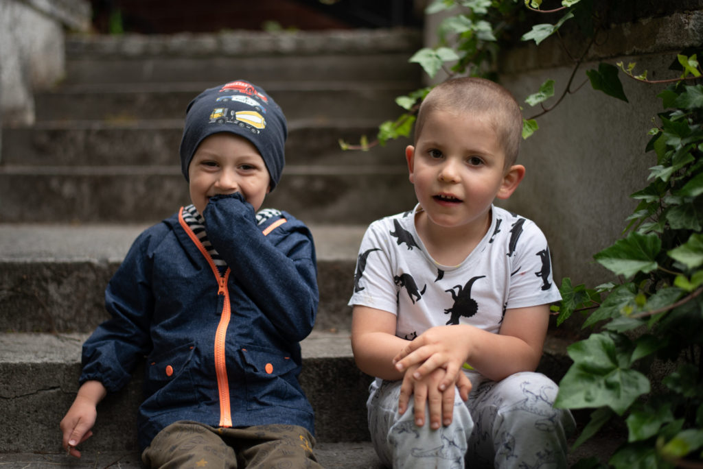 Dwaj uśmiechnięci chłopcy siedzą na kamiennych schodkach w ogrodzie
