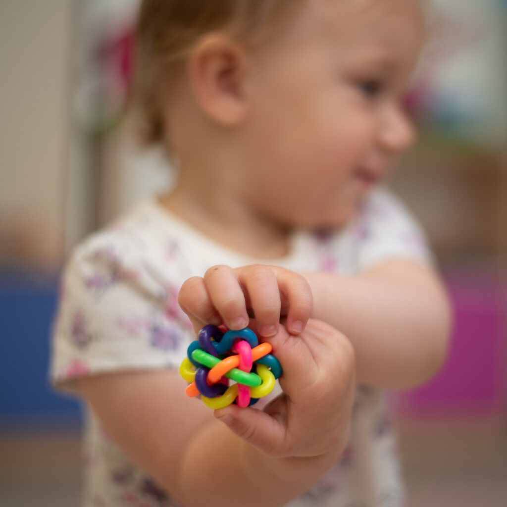 Dziewczynka trzyma w dłoni kolorową zabawkę zrobioną z plastikowych kółek