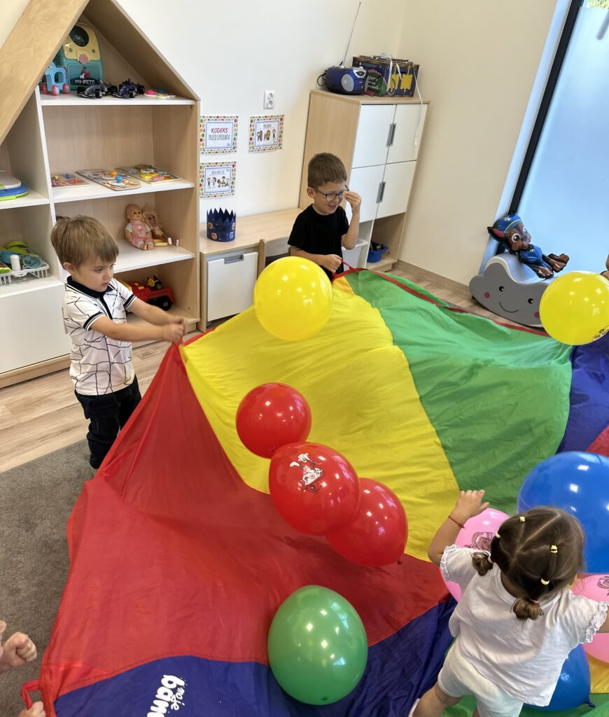 Dzieci bawią się kolorową chustą animacyjną i balonami w sali