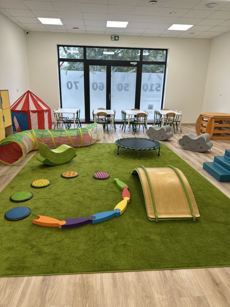Sala ruchowa z zieloną wykładziną, tunelem, trampoliną i miękkimi przeszkodami